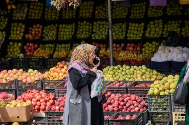 Taşkent, Özbekistan; 16 Eylül 2024: Geleneksel tesettür kullanan yaşlı bir Müslüman kadın, Taşkent, Özbekistan 'da işlek bir meyve pazarında yürürken telefonuyla konuşurken yakalandı. provid