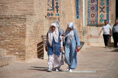 Semerkant, Özbekistan; 18 Eylül 2024: Geleneksel Özbek kıyafetleri ve peçeleriyle Özbekistan 'ın Semerkant kentinin tarihi sokaklarında yürüyen bir anne ve kız.