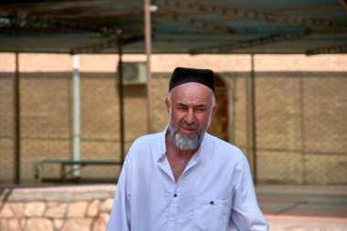 Buhara, Özbekistan; Eylül 19.2024: Özbekistan 'ın Buhara kentinde geleneksel Tyubeteika şapkasını takan beyazlar içinde Özbek bir adamın yakın çekimi.