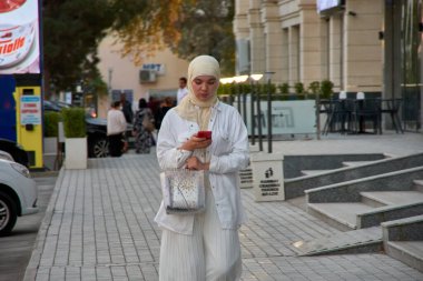 Buhara, Özbekistan; Eylül 19.2024: Beyaz peçe takmış güzel bir Müslüman kadın Özbekistan 'ın Buhara kentinin büyüleyici zeminine karşı duruyor.. 