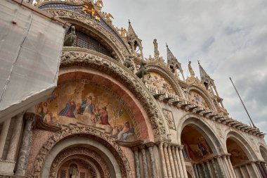 Venedik, İtalya 'daki St. Mark Bazilikası' nın süslü cephesine yakın çekim. Bu ikonik Bizans başyapıtı, İncil 'deki sahneleri, süslemeleri ve bir dizi görkemli kemeri anlatan karmaşık altın mozaikleri sergiliyor..