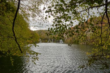 Hırvatistan 'ın Plitvice Lakes Ulusal Parkı' nda sonbaharda meydana gelen küçük şelaleler. Suyun yumuşak akışı kayaların üzerinde hafifçe çağlar, sonbahar yapraklarının canlı renkleriyle çevrilidir. Altın, turuncu ve kırmızı yapraklar kristalle güzel bir kontrast oluşturuyor.