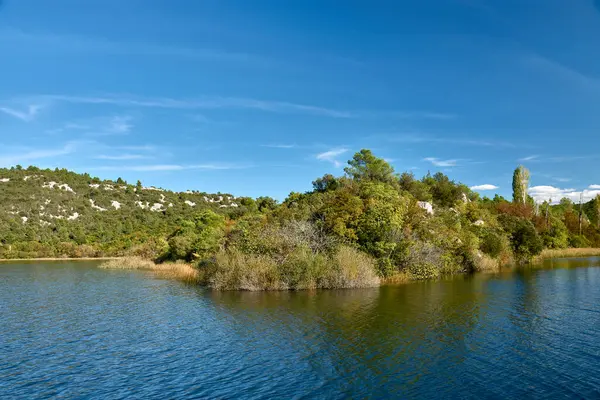 Hırvatistan 'daki Krka Ulusal Parkı' nda huzurlu bir tekne yolculuğu. Teknenin dalgalanması berrak sularda dalgalanır, etrafındaki yemyeşil tepeleri yansıtır ve parlak mavi gökyüzü tüylü beyaz bulutlarla beneklenir..