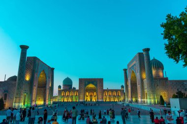 SAMARKAND, UZBEKISTAN - 17 Eylül 2024: Semerkant, Özbekistan 'daki Registan Meydanı, akşam gökyüzünün altında aydınlandı. Tarihi İpek Yolu boyunca önemli bir konum olarak Registan Meydanı üç büyük medresesi ile ünlüdür.