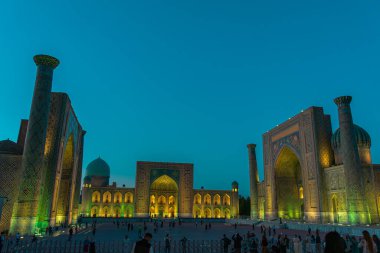 SAMARKAND, UZBEKISTAN - 17 Eylül 2024: Semerkant, Özbekistan 'daki Registan Meydanı, akşam gökyüzünün altında aydınlandı. Tarihi İpek Yolu boyunca önemli bir konum olarak Registan Meydanı üç büyük medresesi ile ünlüdür.