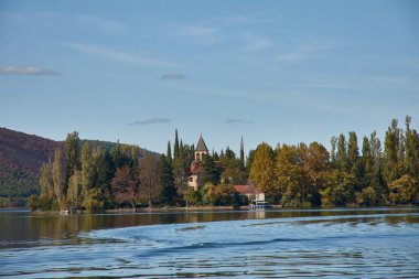 Visovac Island, located in the heart of Krka National Park, Croatia. The island is home to the historic Visovac Monastery, surrounded by lush greenery and calm, reflective waters. Set against a backdrop of hills and forests clipart