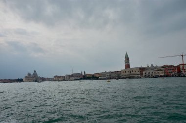 Venedik 'in ikonik silueti, St. Mark' s Campanile 'i ve St. Mark Meydanı' nın tarihi binalarını barındırıyor. Bu sakin görüntü, Venedik gölünün sakin sularını gösteren kenti uzaktan yakalıyor..