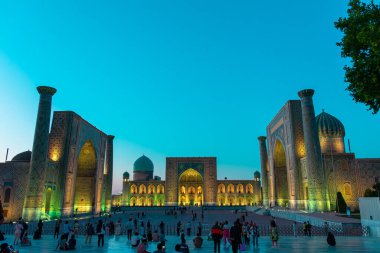 SAMARKAND, UZBEKISTAN - 17 Eylül 2024: Semerkant, Özbekistan 'daki Registan Meydanı, akşam gökyüzünün altında aydınlandı. Tarihi İpek Yolu boyunca önemli bir konum olarak Registan Meydanı üç büyük medresesi ile ünlüdür.