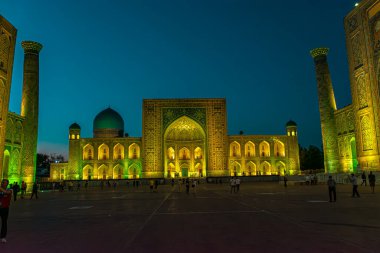 SAMARKAND, UZBEKISTAN - 17 Eylül 2024: Semerkant, Özbekistan 'daki Registan Meydanı, akşam gökyüzünün altında aydınlandı. Tarihi İpek Yolu boyunca önemli bir konum olarak Registan Meydanı üç büyük medresesi ile ünlüdür.