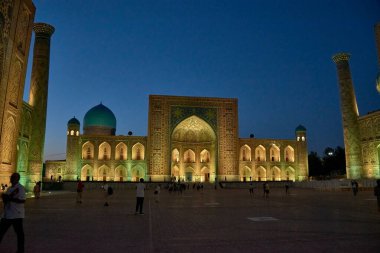 SAMARKAND, UZBEKISTAN - 17 Eylül 2024: Semerkant, Özbekistan 'daki Registan Meydanı, akşam gökyüzünün altında aydınlandı. Tarihi İpek Yolu boyunca önemli bir konum olarak Registan Meydanı üç büyük medresesi ile ünlüdür.