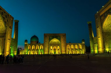 SAMARKAND, UZBEKISTAN - 17 Eylül 2024: Semerkant, Özbekistan 'daki Registan Meydanı, akşam gökyüzünün altında aydınlandı. Tarihi İpek Yolu boyunca önemli bir konum olarak Registan Meydanı üç büyük medresesi ile ünlüdür.
