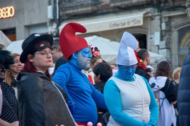 Vigo, Pontevedra, İspanya; 4 Mart 2025: Şirin gibi giyinmiş bir adam İspanya 'daki canlı Vigo Karnavalı' nda kalabalığın arasında duruyor. Yüzü tamamen maviye boyanmış ve çok sevdiği karakterin özünü yansıtan ikonik kırmızı bir şapka takıyor.. 