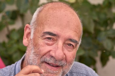 Kel, yarı beyaz sakallı, sıkıntısını ve yorgunluğunu ifade eden olgun bir adamın yakın plan görüntüsü. Samimi ifadesi yorgunluk, monotonluk ve günlük insan duygularını vurguluyor.. 