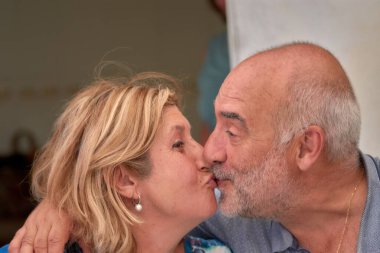 Sevecen, yaşlı bir çiftin öpüşmesinin yakın plan görüntüsü. Erkek ve kadın, hem olgun hem de anlamlı, bir anlık sevgi ve bağ sergilerler..