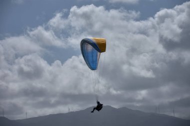 İspanya, Asturias 'ta, Coana' da, Faro de San Agustin üzerinde nefes kesici bir uçuş gerçekleştiren bir paraglider. Dramatik bulutlu bir gökyüzüne yakalanan sahne, İspanya 'nın kuzeyindeki ekstrem sporların ve açık hava maceralarının güzelliğini vurguluyor. tur