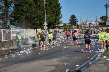 Nigran, Pontevedra, İspanya; 6 Nisan 2025: Yüksek görüşlü yelek giyen genç gönüllüler, İspanya 'nın Nigrn kentindeki Vig Bay Yarı Maratonu sırasında koşuculara suya batırılmış süngerler dağıtıyor. 