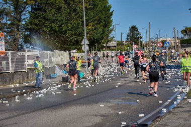 Nigran, Pontevedra, İspanya; 6 Nisan 2025: Yüksek görüşlü yelek giyen genç gönüllüler, İspanya 'nın Nigrn kentindeki Vig Bay Yarı Maratonu sırasında koşuculara suya batırılmış süngerler dağıtıyor. 