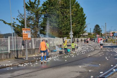 Nigran, Pontevedra, İspanya; 6 Nisan 2025: Yüksek görüşlü yelek giyen genç gönüllüler, İspanya 'nın Nigrn kentindeki Vig Bay Yarı Maratonu sırasında koşuculara suya batırılmış süngerler dağıtıyor. 