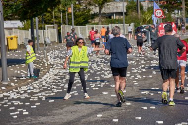 Nigran, Pontevedra, İspanya; 6 Nisan 2025: Yüksek görüşlü yelek giyen genç gönüllüler, İspanya 'nın Nigrn kentindeki Vig Bay Yarı Maratonu sırasında koşuculara suya batırılmış süngerler dağıtıyor. 