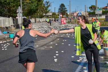 Nigran, Pontevedra, İspanya; 6 Nisan 2025: Yüksek görüşlü yelek giyen genç gönüllüler, İspanya 'nın Nigrn kentindeki Vig Bay Yarı Maratonu sırasında koşuculara suya batırılmış süngerler dağıtıyor. 