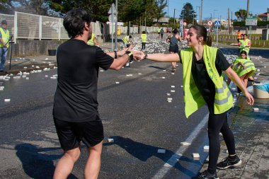 Nigran, Pontevedra, İspanya; 6 Nisan 2025: Yüksek görüşlü yelek giyen genç gönüllüler, İspanya 'nın Nigrn kentindeki Vig Bay Yarı Maratonu sırasında koşuculara suya batırılmış süngerler dağıtıyor. 