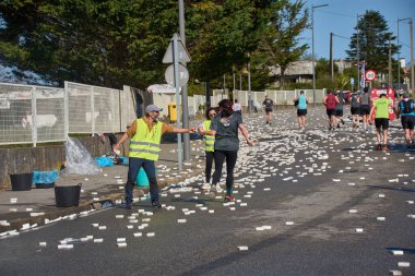 Nigran, Pontevedra, İspanya; 6 Nisan 2025: Yüksek görüşlü yelek giyen genç gönüllüler, İspanya 'nın Nigrn kentindeki Vig Bay Yarı Maratonu sırasında koşuculara suya batırılmış süngerler dağıtıyor. 