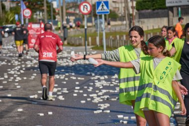Nigran, Pontevedra, İspanya; 6 Nisan 2025: Yüksek görüşlü yelek giyen genç gönüllüler, İspanya 'nın Nigrn kentindeki Vig Bay Yarı Maratonu sırasında koşuculara suya batırılmış süngerler dağıtıyor. 