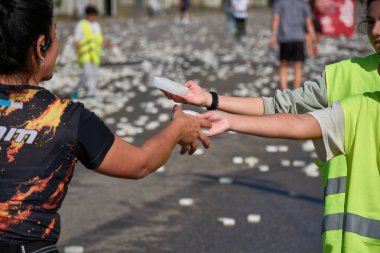 Nigran, Pontevedra, İspanya; 6 Nisan 2025: Yüksek görüşlü yelek giyen genç gönüllüler, İspanya 'nın Nigrn kentindeki Vig Bay Yarı Maratonu sırasında koşuculara suya batırılmış süngerler dağıtıyor. 