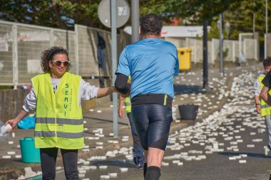Nigran, Pontevedra, İspanya; 6 Nisan 2025: Yüksek görüşlü yelek giyen genç gönüllüler, İspanya 'nın Nigrn kentindeki Vig Bay Yarı Maratonu sırasında koşuculara suya batırılmış süngerler dağıtıyor. 