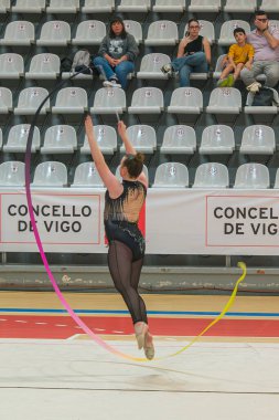 Vigo, Pontevedra, İspanya; 12 Nisan 2025; yetenekli bir jimnastikçi modern Vigo Belediye Spor Salonu 'nda zarif bir şekilde ritmik jimnastik kurdele egzersizleri yapar. Akışkan hareketleri ve kusursuz kontrolü bu disiplinin güzelliğini vurguluyor..