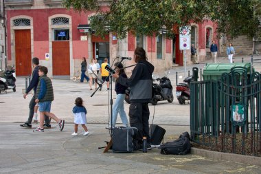 Vigo, Pontevedra, İspanya, 1 Mayıs 2025, Vigo, İspanya 'da ünlü bir zeytin ağacının gölgesinde akustik gitarını çalan bir sokak müzisyeni. Yoldan geçenler arka planda geziniyor, şehrin keyifli bir gününde canlı müziğin tadını çıkarıyorlar.. 