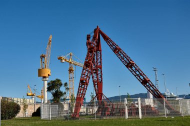 Görüntü, İspanya, Vigo 'da eski ve sağlam bir kırmızı liman vincinin şehrin zengin tersane tarihi anısına dikildiği bir kavşağı yakalıyor.. 