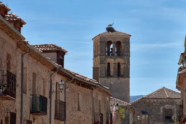 Pedraza 'nın kilisesinin görkemli taş çan kulesi etrafındaki evlerin kiremitli çatılarının üzerinde belirgin bir şekilde yükselir, açık mavi gökyüzünün altında bir leylek yuvası bulunur.. 