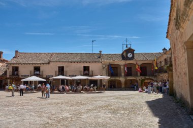 Pedraza, Segovia, İspanya; 24 Mayıs 2025: Pedraza 'nın kaldırım taşlarıyla döşenmiş ikonik Plaza Belediye Başkanı, ahşap balkonlu geleneksel taş evlerle çevrili, açık mavi gökyüzü altında güneşli terasların keyfini çıkaran insanlarla dolup taşıyor.. 