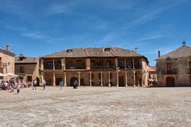 Pedraza, Segovia, İspanya; 24 Mayıs 2025: Pedraza 'nın kaldırım taşlarıyla döşenmiş ikonik Plaza Belediye Başkanı, ahşap balkonlu geleneksel taş evlerle çevrili, açık mavi gökyüzü altında güneşli terasların keyfini çıkaran insanlarla dolup taşıyor.. 