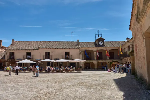 Pedraza, Segovia, İspanya; 24 Mayıs 2025: Pedraza 'nın kaldırım taşlarıyla döşenmiş ikonik Plaza Belediye Başkanı, ahşap balkonlu geleneksel taş evlerle çevrili, açık mavi gökyüzü altında güneşli terasların keyfini çıkaran insanlarla dolup taşıyor.. 