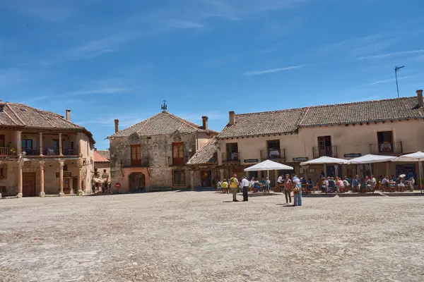 Pedraza, Segovia, İspanya; 24 Mayıs 2025: Pedraza 'nın kaldırım taşlarıyla döşenmiş ikonik Plaza Belediye Başkanı, ahşap balkonlu geleneksel taş evlerle çevrili, açık mavi gökyüzü altında güneşli terasların keyfini çıkaran insanlarla dolup taşıyor.. 
