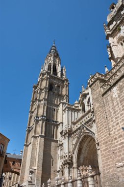 Toledo Katedrali Ayuntamiento Meydanı 'ndan alınan parlak mavi gökyüzünün altında görkemli bir şekilde duruyor. Sıcak taş tonlar, gotik kubbe ve barok kubbe görsel olarak zengin ve tarihsel açıdan önemli bir kompozisyon oluşturur.