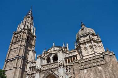 Toledo Katedrali Ayuntamiento Meydanı 'ndan alınan parlak mavi gökyüzünün altında görkemli bir şekilde duruyor. Sıcak taş tonlar, gotik kubbe ve barok kubbe görsel olarak zengin ve tarihsel açıdan önemli bir kompozisyon oluşturur.