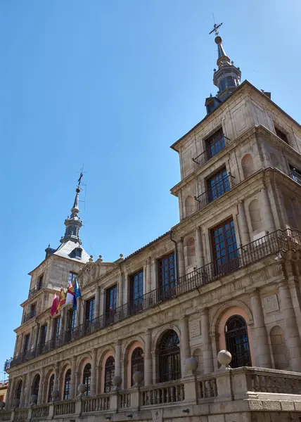 Rönesans tarzı Toledo belediye binası ulusal ve bölgesel bayraklarla süslenmiş canlı mavi gökyüzüne karşı simetri ve zarafetle yükseliyor. Sıcak taş tonları ve klasik çizgiler, toplumsal gurur ve mimari mirası yansıtıyor.