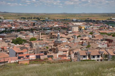Consuegra, Toledo 'nun geniş açılı bir manzarası, kırmızı kiremitli çatılar, tarihi bir kilise ve dağınık bulutlarla kaplı mavi gökyüzünün altındaki tarım arazilerini gösteriyor. Sıcak melodiler ve açık mekan huzurlu bir ortam oluşturuyor.