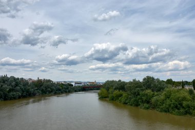 Guadalquivir Nehri, Crdoba 'nın anıtsal silueti tarafından çerçevelenmiş Roma Köprüsü' nün altında dönüyordu. Bileşim, suyun hareketini tarihi mimarinin sağlamlığıyla dengeler.