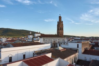 Llerena, Badajoz 'un tarihi merkezinin genel manzarası. Granada Kilisesi' nin görkemli Mudejar kulesi, kırmızı çatı ve duvarlara karşı duruyor. Sıcak bir günbatımı ışığı altında.. 