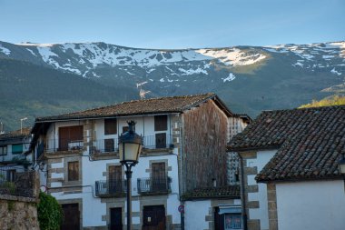 Salamanca, Candelario köyünde kiremitli çatıları ve taş ve ahşap cepheleri olan geleneksel evler, açık bir gökyüzünün altında ve arka planda kısmen karla kaplı dağlarla birlikte.. 