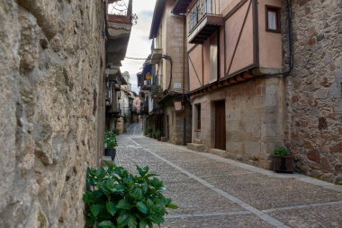 Görüntü, Salamanca 'nın Miranda del Castaar kasabasında ahşap detaylar ve balkonlarla çevrili taş binalar ve cephelerle çevrili bir kaldırım taşı sokağını tasvir ediyor.. 