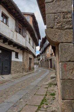 La Alberca 'da balkonları ve pencereleri saksı ve çiçeklerle süslenmiş geleneksel taş ve yarı keresteli evlerle çevrili kaldırımlı bir sokak. Kompozisyon, İspanya 'nın ilk tarihi-sanatsal mekanının kırsal cazibesini ve tarihini vurguluyor.
