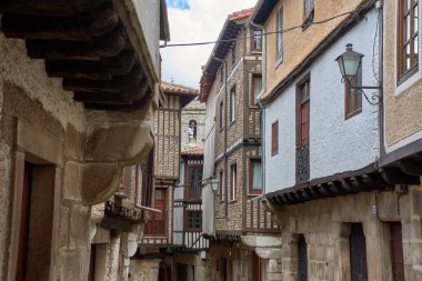 La Alberca 'da balkonları ve pencereleri saksı ve çiçeklerle süslenmiş geleneksel taş ve yarı keresteli evlerle çevrili kaldırımlı bir sokak. Kompozisyon, İspanya 'nın ilk tarihi-sanatsal mekanının kırsal cazibesini ve tarihini vurguluyor.