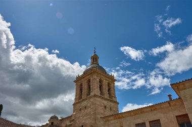 Salamanca 'daki Ciudad Rodrigo Katedrali' nin bir kısmı, bulutlu bir gökyüzünün altındaki yeşil ağaçların arasında duran Roma tarzı kulesi. Taşın ılık tonları Skyatmoshe 'nin gri ve mavisi ile tezat oluşturuyor.