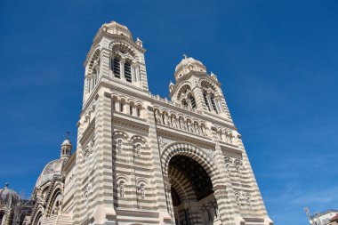 Marsilya Katedrali, Sainte-Marie-Majeure, büyük taş kubbeleri ve iki tonluk kuleleriyle yükseliyor, La Joliette mahallesindeki neo-Bizans tarzının anıtsallığını vurguluyor.. 