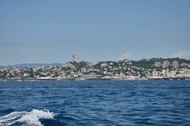 Bir teknenin bakış açısından, Marsilya 'nın ikonik limanı şehrin tarihi mimarisi ve derin mavi gökyüzü tarafından çerçevelenmiş yatlar ve yelkenlilerle doludur. Kompozisyon sükuneti iletiyor ve Akdeniz atmosferini çağrıştırıyor, 